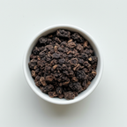 Dried black walnut hull cut and sifted pieces in a white ceramic bowl on a white background