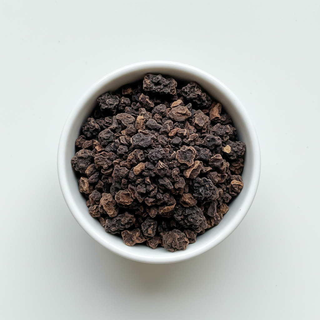Dried black walnut hull cut and sifted pieces in a white ceramic bowl on a white background