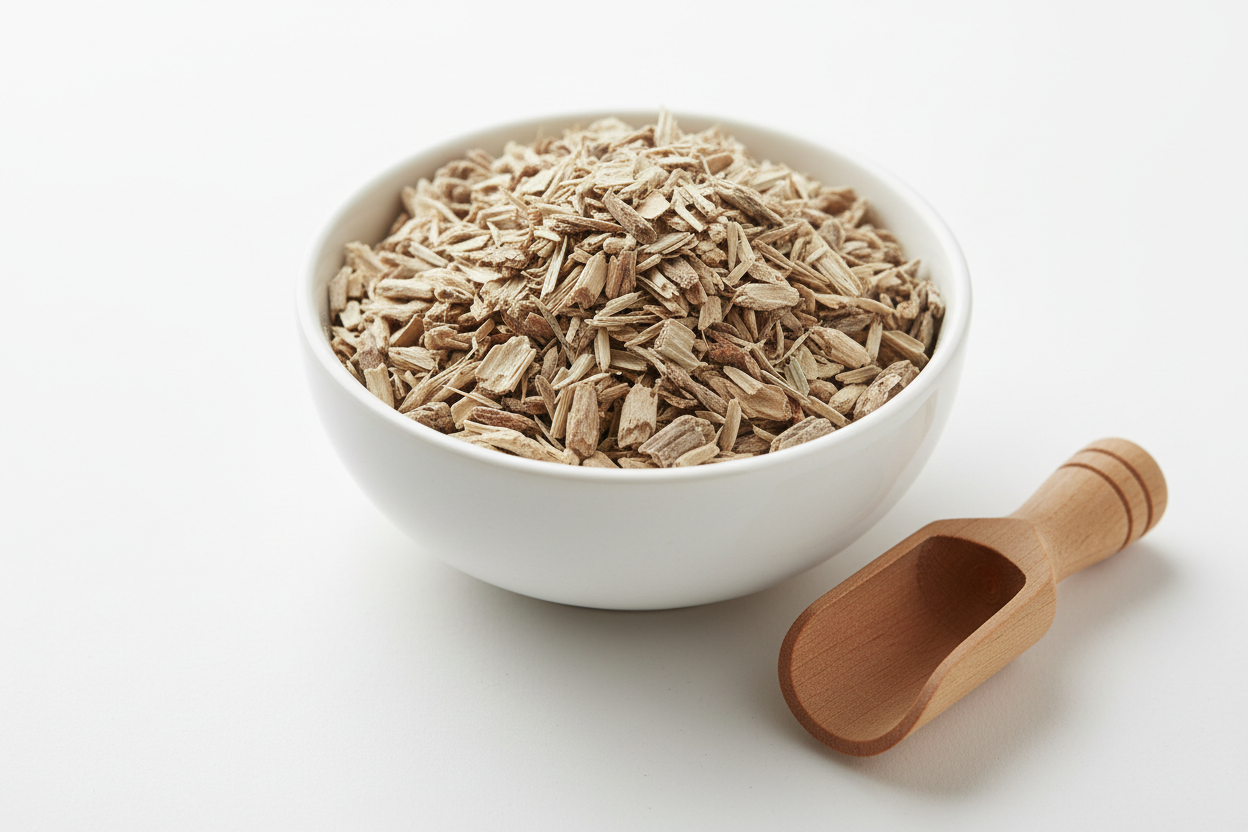 Dried white willow bark cut and sifted pale tan fibrous bark pieces in a white ceramic bowl with wooden scoop