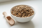 Dried elecampane rhizome cut and sifted tan brown woody root pieces in a white ceramic bowl with wooden scoop