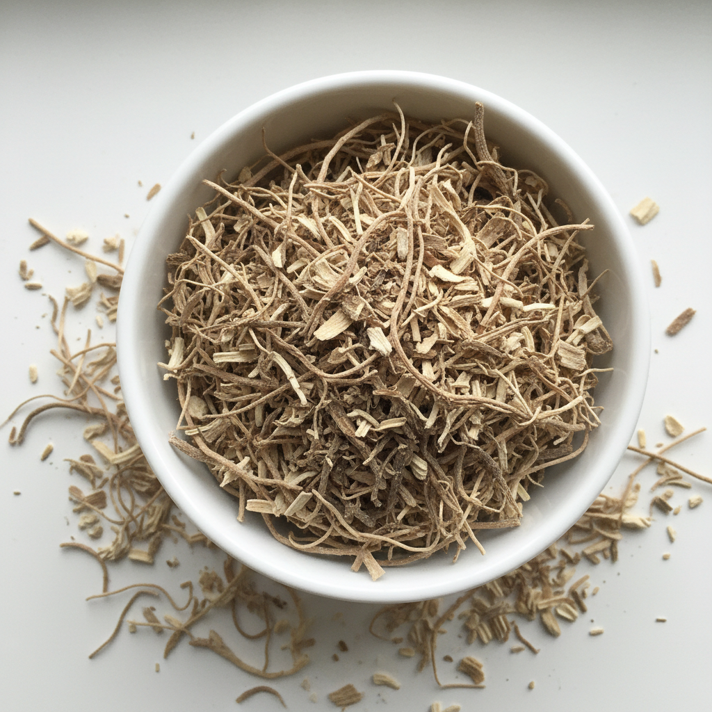 Dried nettle root cut and sifted — thin fibrous stringy pieces in a white ceramic bowl with some scattered on white surface